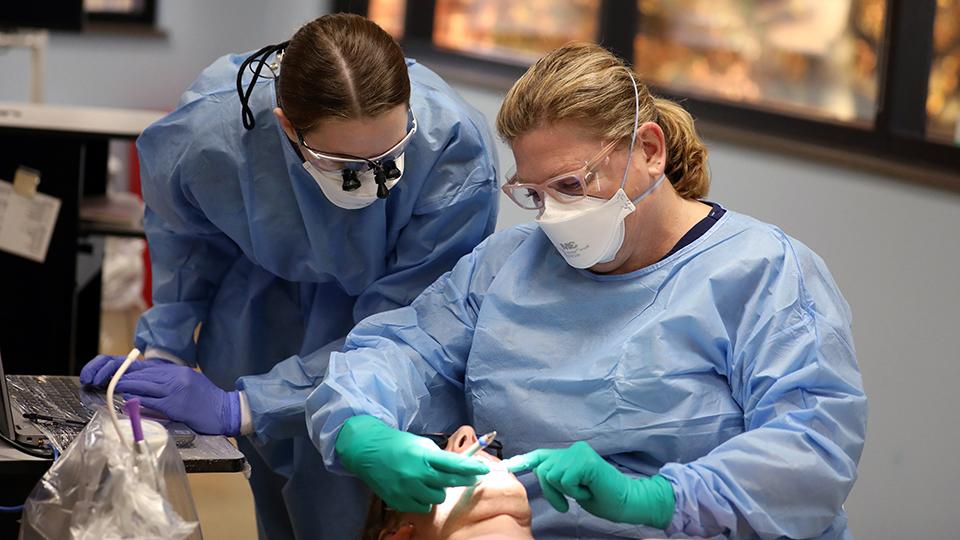 An instructor supervises a student doing a dental cleaning on a patient.