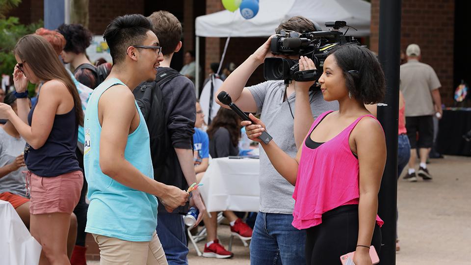 Students with a camera and microphone interview another student.