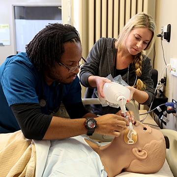 Two respiratory care students works on a manikin.