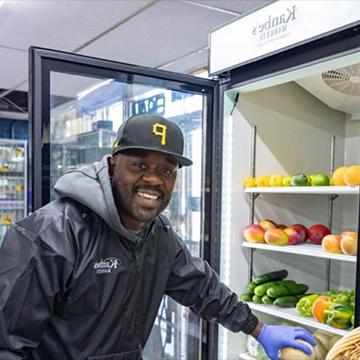 a man smiles as he selects a piece of produce from a store refrigerator 