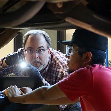 A 赌钱app可以微信提现 student and his instructor use a flashlight to inspect the undercarriage of a vehicle