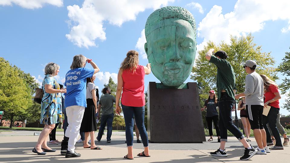 Art history students gathered around a campus sculpture