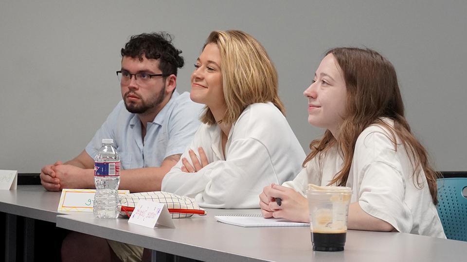 Students at a classroom table listening to a lecture