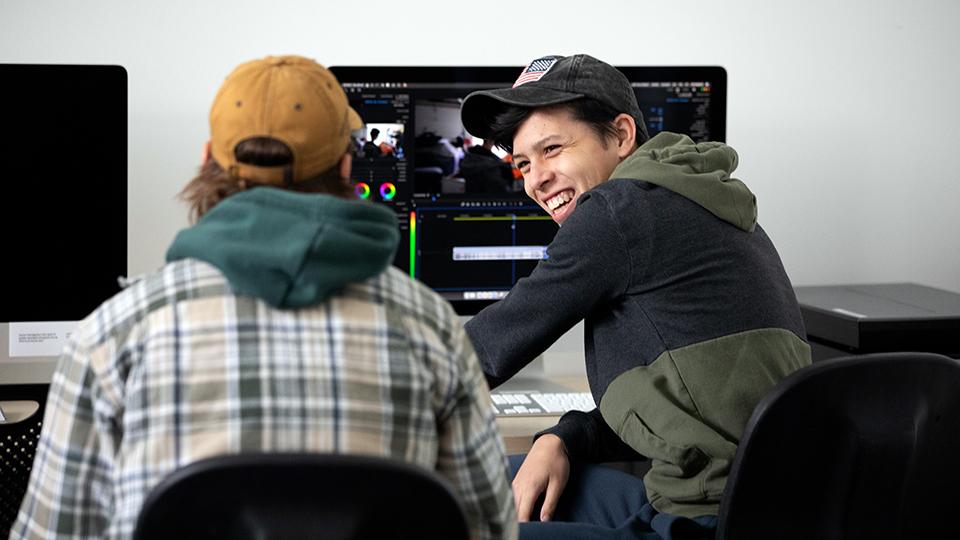 Two students laughing while working with film editing software on a computer