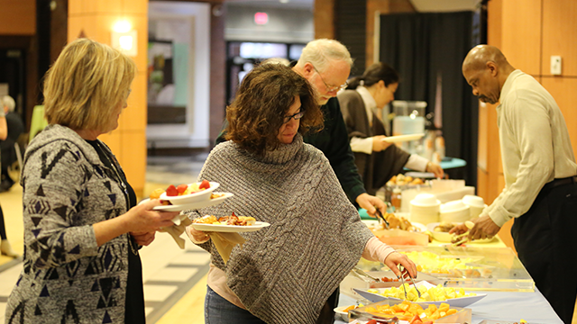 Buffet table with a variety of breakfast dishes. People are in line and serving themselves.