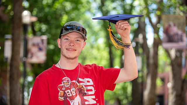 Spencer Nemecek holding up a J C C C graduation cap.