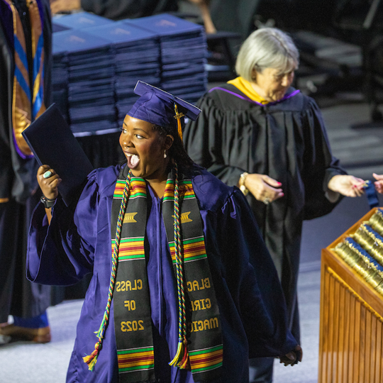 Graduate wearing a stole waving and grinning at attendees