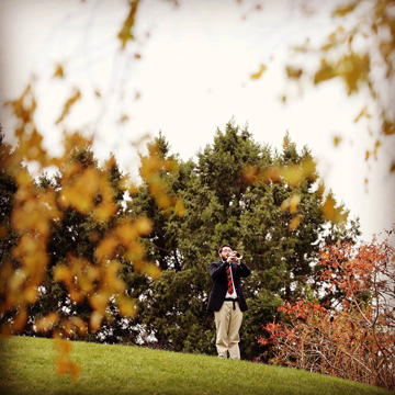 Student veteran playing taps on a bugle surround by fall foliage