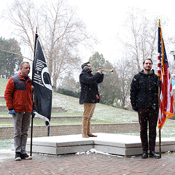 Flag bearers on either side of a student veteran bugler; snow is falling